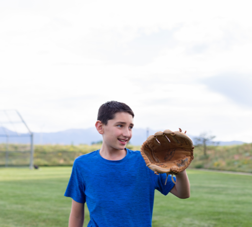 A young boy holds up a baseball mitt in a field