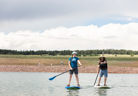 Two people stand on paddle boards in the middle of a lake