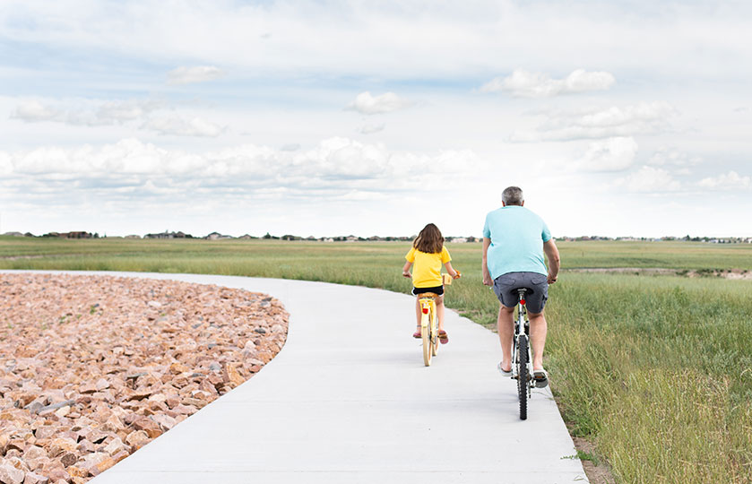 A man and a girl ride bikes together down a sidewalk